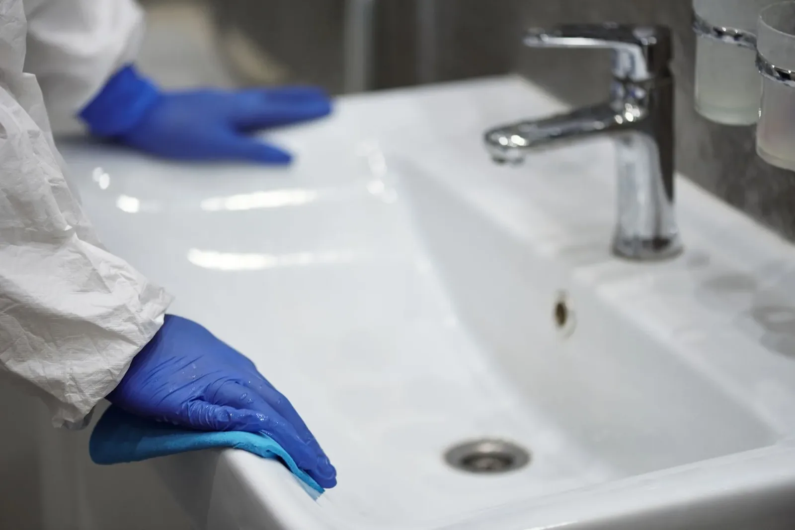 Gloved hands cleaning a white washbasin